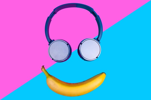 Concetto piatto pop art di banana e cuffie su sfondo colorato vivido che forma una faccia sorridente. Stile piatto e colori