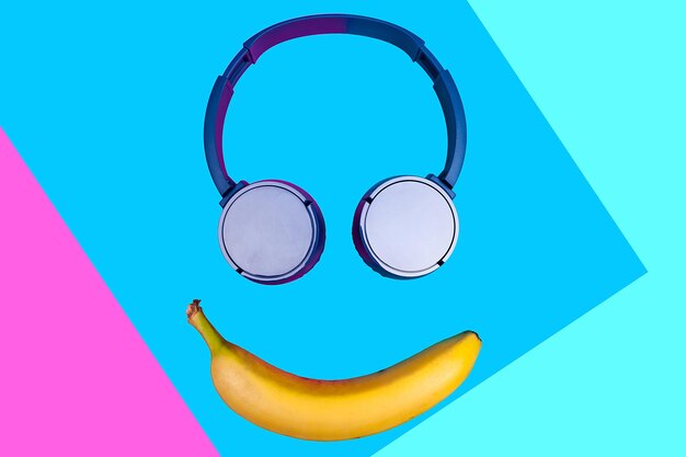 Concetto piatto pop art di banana e cuffie su sfondo colorato vivido che forma una faccia sorridente. Stile piatto e colori