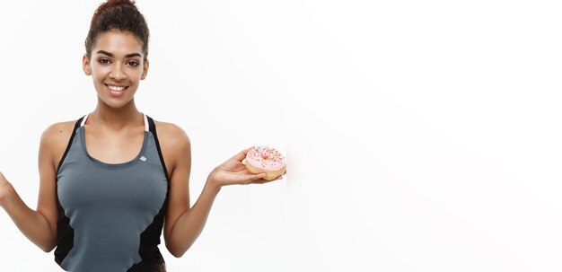 Concetto sano e dietetico Il bellissimo afroamericano sportivo prende una decisione tra ciambella e verde