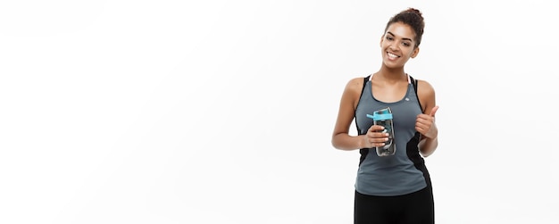 Concetto sano e fitness bella ragazza afroamericana in abiti sportivi tenendo una bottiglia d'acqua dopo l'allenamento isolato su sfondo bianco per studio