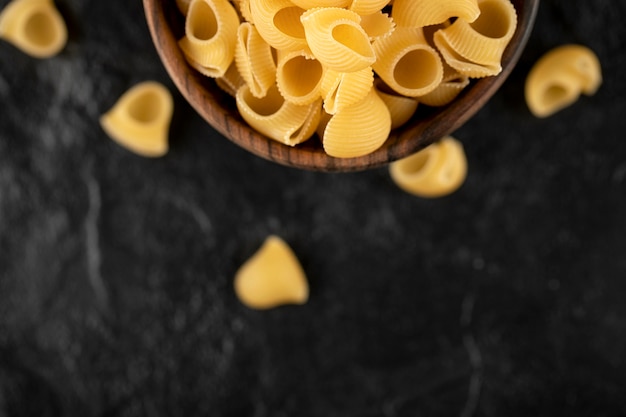 Conchiglie di pasta cruda italiana nella ciotola di legno.