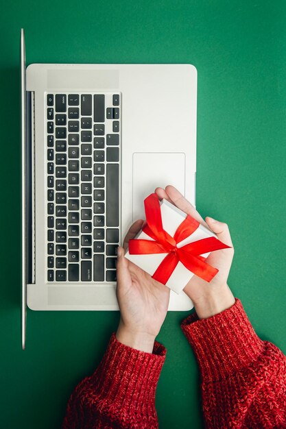 Confezione regalo in mani femminili e laptop online Concetto di shopping natalizio