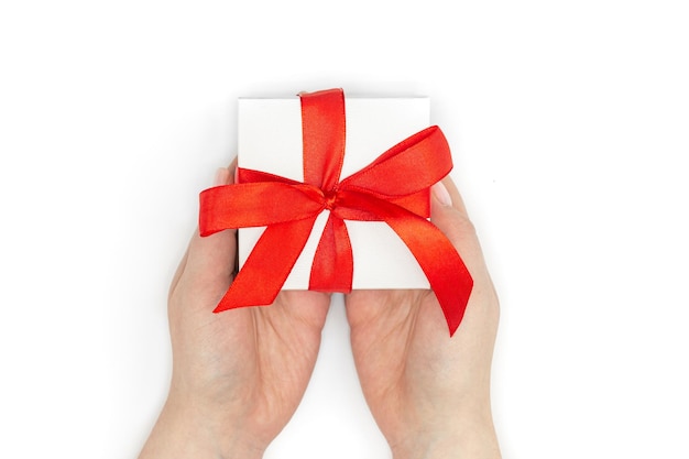 Confezione regalo in un nastro rosso in mani femminili su sfondo bianco vista dall'alto