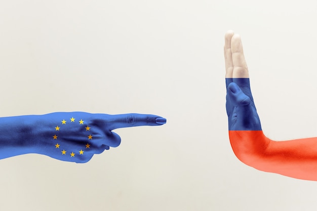 Confronto, disaccordo tra paesi. Mani femminili e maschili colorate in bandiere di unità europea e Russia isolato su sfondo grigio. Concetto di aggressioni politiche, economiche o sociali.