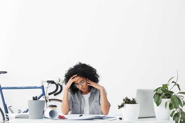 Confusa donna di razza mista concentrata vestita formalmente indossando grandi occhiali rotondi