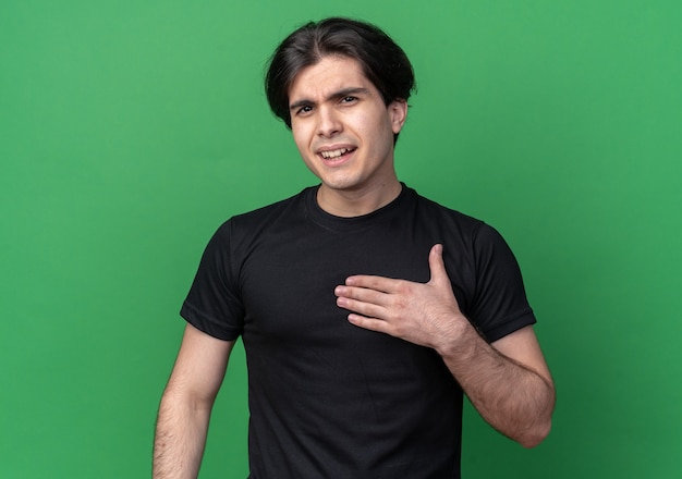 Confuso giovane bel ragazzo che indossa la maglietta nera mettendo la mano su se stesso isolato sulla parete verde