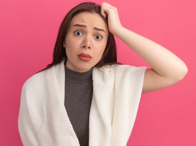 Confuso giovane bella donna che tiene la mano sulla testa isolata sul muro rosa