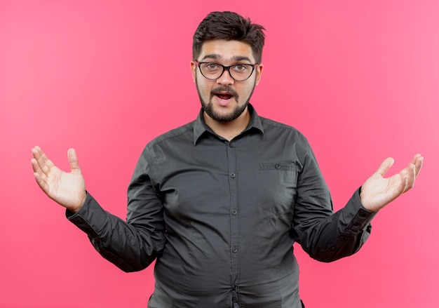 Confuso giovane imprenditore con gli occhiali diffonde le mani isolate sulla parete rosa