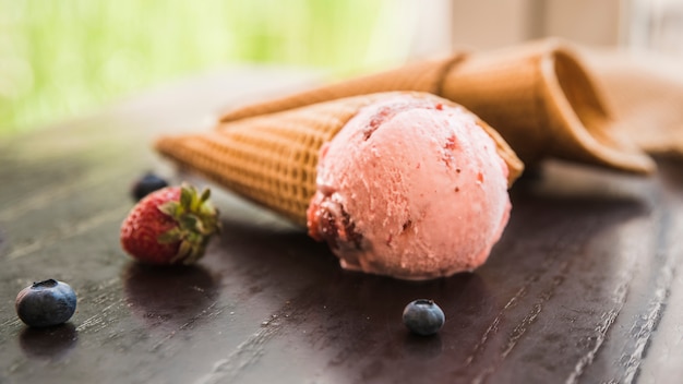 Coni della cialda con il gelato vicino alle bacche fresche sulla tavola