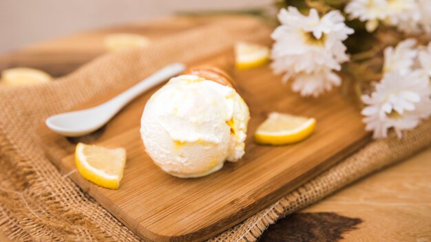 Cono di cialda con gelato vicino a fette di frutta fresca e fiori a bordo