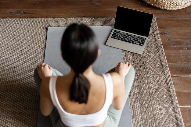 Consapevolezza e meditazione concetto vista posteriore di una giovane donna asiatica che medita a casa seguendo online...