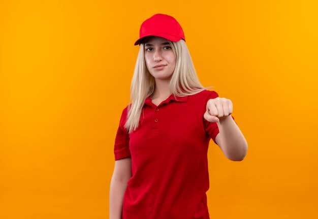 consegna giovane donna che indossa t-shirt rossa e berretto tendendo il pugno sulla parete arancione isolata