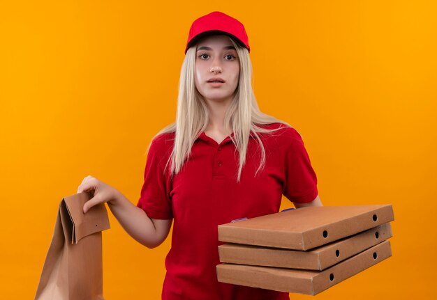 consegna giovane donna che indossa t-shirt rossa e cappuccio tenendo la tasca della carta e la scatola della pizza sulla parete arancione isolata