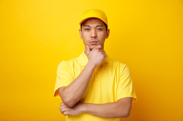 Considerato giovane uomo di consegna che indossa il cappello e uniforme tenendo la mano sul mento