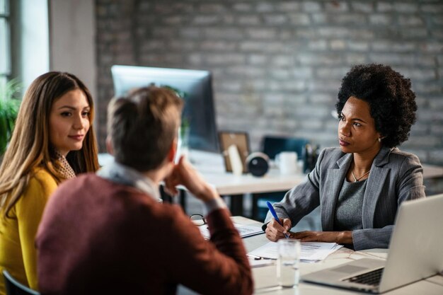 Consulente finanziario afroamericano che scrive relazioni durante un incontro con i clienti in ufficio