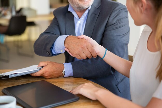 Consulente legale maturo incontro con un giovane cliente in co-working, tenendo documenti e stringendo la mano