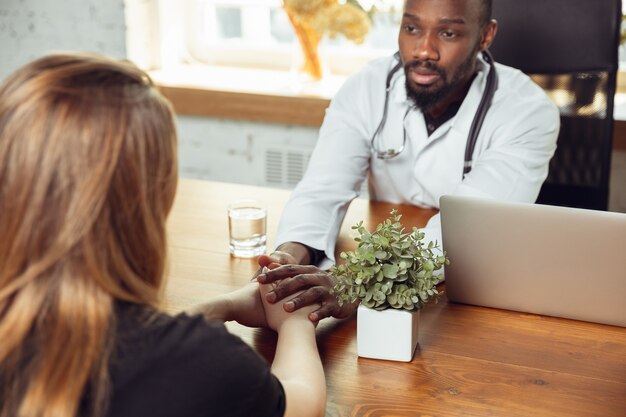 Consulenza medica per paziente femminile nell'armadietto. Medico afroamericano durante il suo lavoro con i pazienti, spiegando le ricette per la droga. Duro lavoro quotidiano per la salute e il salvataggio di vite durante l'epidemia.