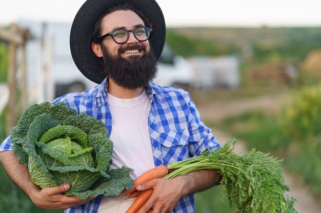 Contadino che abbraccia verdure fresche con le mani sorridenti che tengono carote e cavoli. Prepararsi per la consegna ecologica biologica