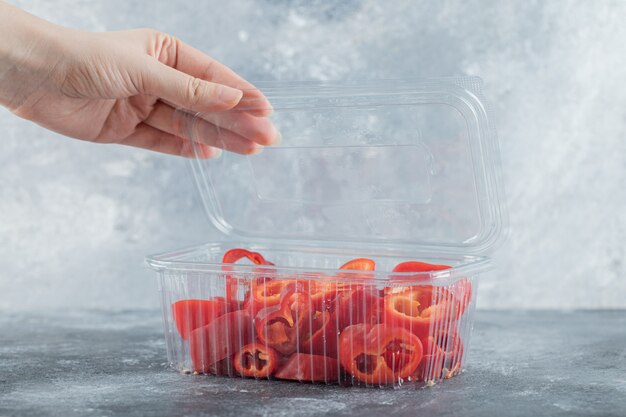 Contenitore di plastica con apertura a mano femminile, contenitore di plastica pieno di peperoni rossi a fette