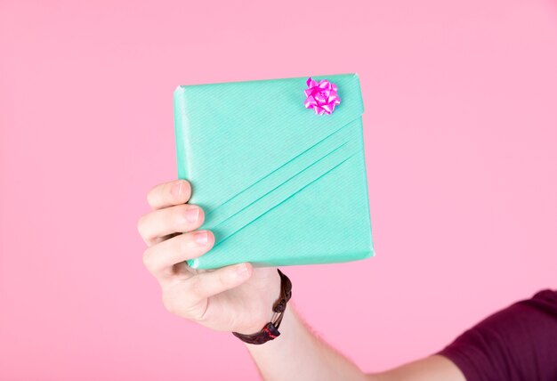 Contenitore di regalo del turchese avvolto tenuta della mano dell'uomo su fondo rosa