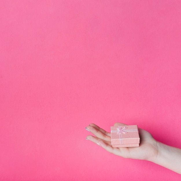 Contenitore di regalo sulla mano della palma della femmina contro fondo bianco