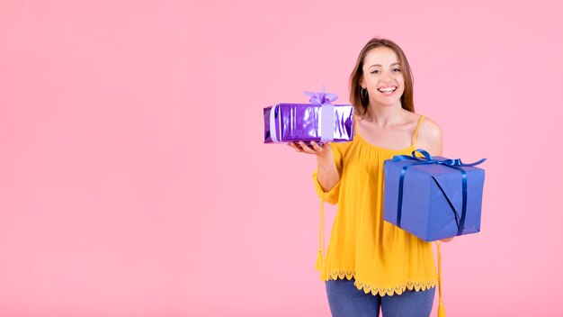 Contenitori di regalo felici della tenuta della giovane donna contro fondo rosa