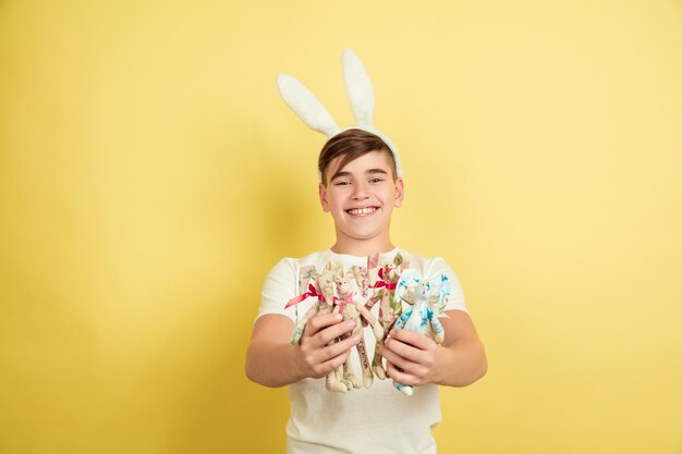 Contento. Decorare. Ragazzo caucasico come un coniglietto di Pasqua su sfondo giallo studio. Auguri di buona Pasqua. Bellissimo modello maschile. Concetto di emozioni umane, espressione facciale, vacanze. Copyspace.