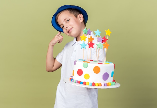 contento giovane ragazzo slavo con blue party hat tenendo la torta di compleanno e gesticolando chiamami segno isolato su verde oliva parete con spazio di copia