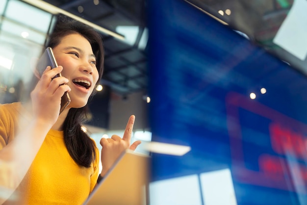 Conversazione di panno casual femminile asiatico dell'agenzia creativa con smartphone freelance che lavora con il laptop nello spazio ufficio dell'area di coworking con freschezza con sfocatura dello sfondo dell'ufficio