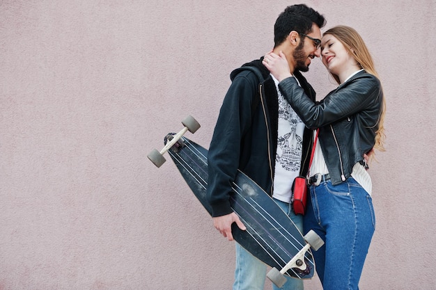 Cool multirazziale coppia in posa contro il muro rosa con longboard