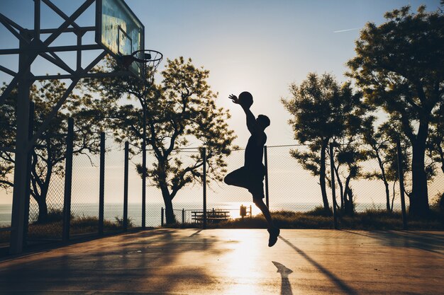 Cool uomo nero facendo sport, giocando a basket all'alba, saltando la sagoma