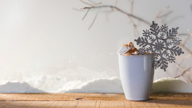 Coppa con fiocco di neve giocattolo sul tavolo di legno vicino banca di neve