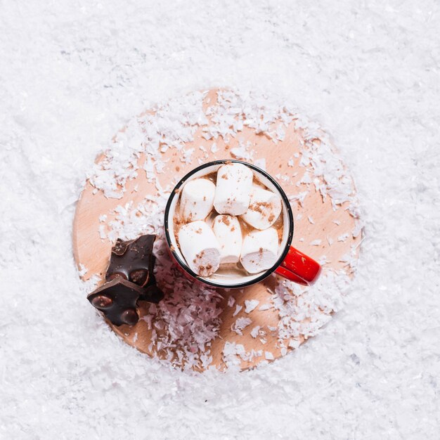 Coppa con marshmallow vicino al cioccolato in stand tra la neve