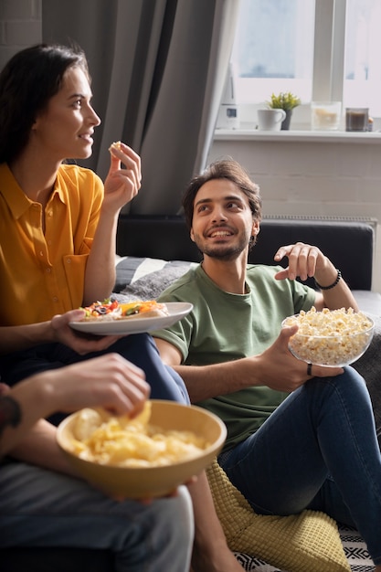 Coppia a casa sul divano gustando popcorn e patatine