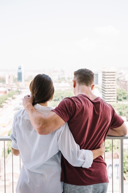 Coppia abbracciare e guardando città dal balcone