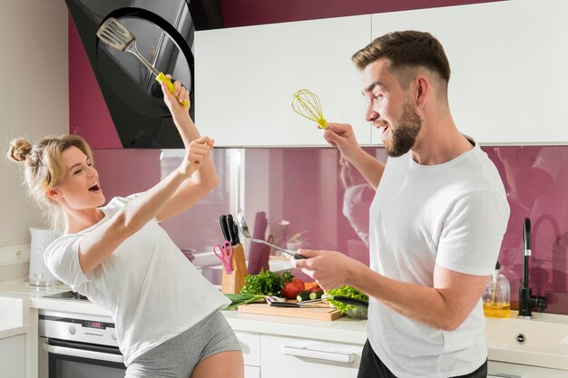 Coppia al chiuso scherzando in cucina con oggetti