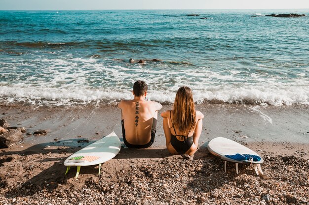 Coppia anonima con tavole da surf guardando mare agitato