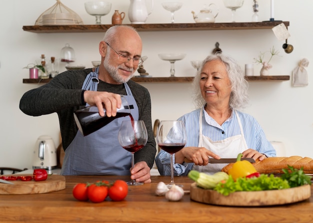 Coppia anziana che cucina insieme in cucina e beve vino