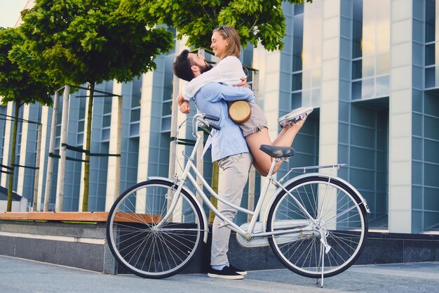 Coppia attraente ad un appuntamento dopo un giro in bicicletta in una città. Un uomo abbraccia una donna su sfondo di un edificio moderno.