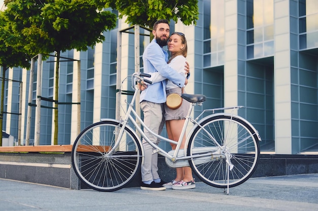 Coppia attraente ad un appuntamento dopo un giro in bicicletta in una città. Un uomo abbraccia una donna su sfondo di un edificio moderno.