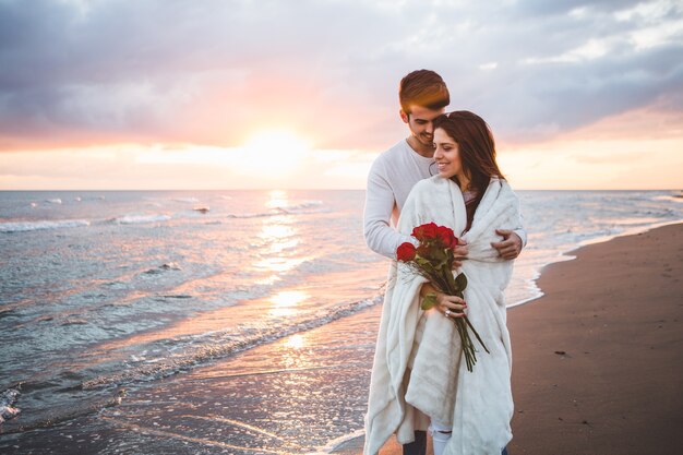 Coppia camminare sulla spiaggia con un mazzo di rose al tramonto