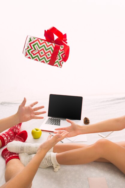 coppia caucasica con regalo. Laptop e telefono per le persone sedute sul pavimento a calzini colorati. Natale, amore, concetto di stile di vita