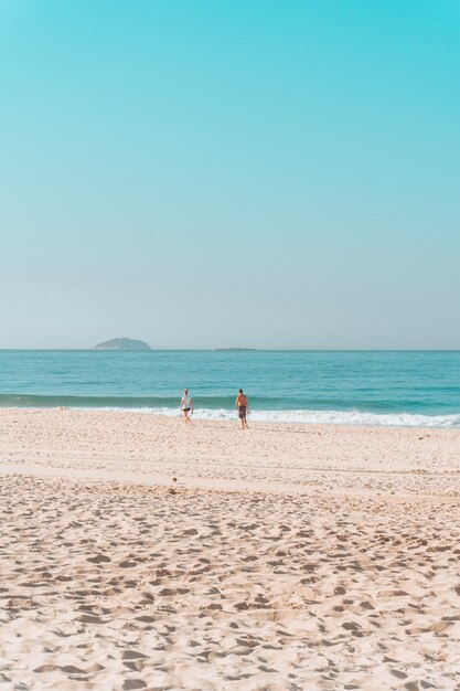 Coppia che cammina lungo la riva su una spiaggia assolata con un cielo senza nuvole sopra