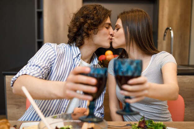 Coppia che si bacia a casa in cucina con bicchieri di vino