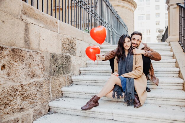 Coppia con palloncini a forma di cuore che guarda l&#39;obbiettivo