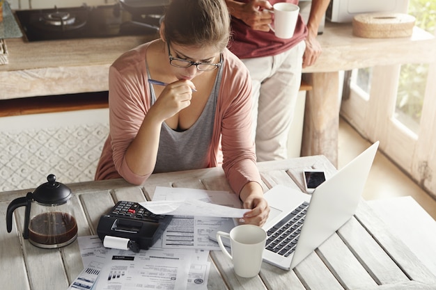 Coppia con problemi di debito, incapace di pagare il mutuo. Donna premurosa che sembra frustrata, tenendo la penna mentre gestiva il bilancio familiare, effettuando i calcoli facendo uso del calcolatore e del pc del taccuino