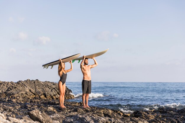 Coppia con tavole da surf sulle teste in piedi vicino al mare