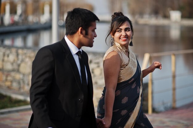 Coppia di amici indiani eleganti e alla moda di donna in sari e uomo in giacca e cravatta che camminano insieme e si tengono per mano