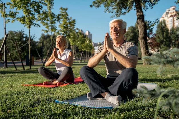 Coppia di anziani a praticare yoga all'esterno