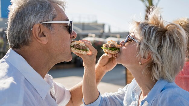 Coppia di anziani godendo di mangiare un hamburger all'aperto